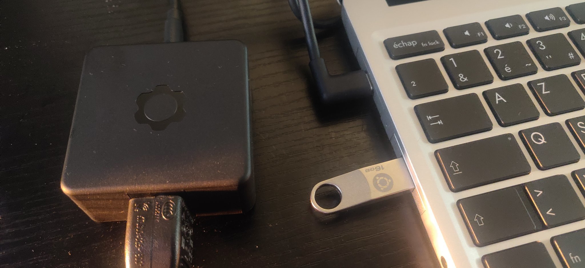 Une clef siglée Ubuntu dans un port USB A de l’ordinateur. À côté, le bloc d’alimentation, portant lui le logo de Frame.work.