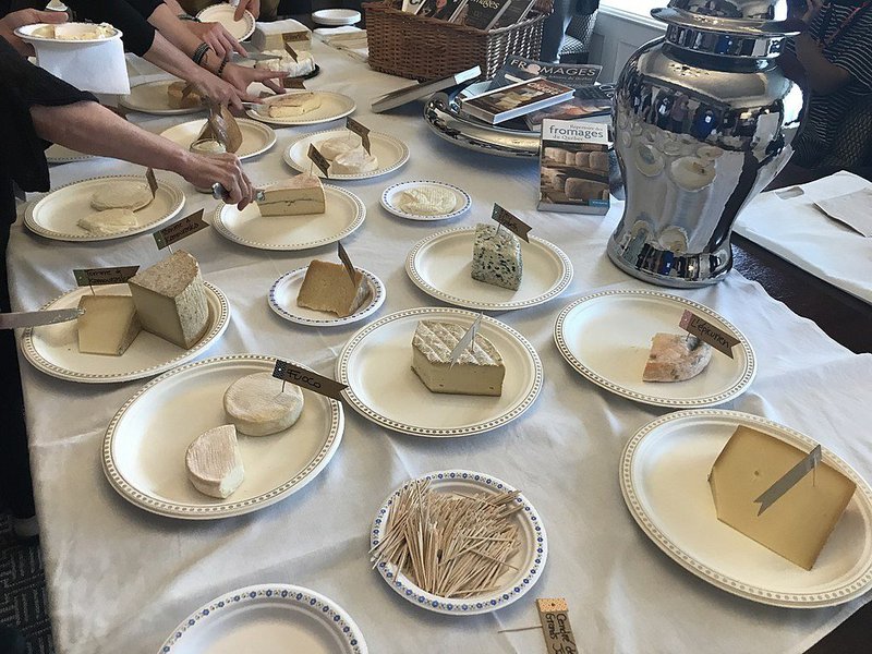 Photo d'une table chargée d'assiettes contenant chacune un fromage différent, avec une petite étiquette indiquant son nom